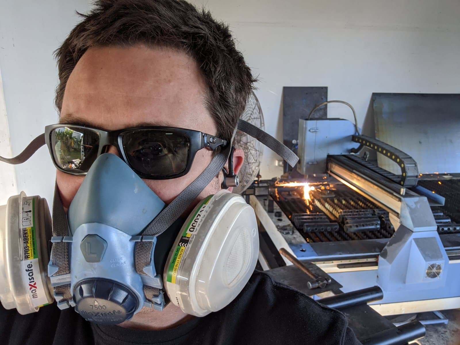 Gunners in a respirator and safety glasses beside a CNC plasma table, sparks coming off the cut